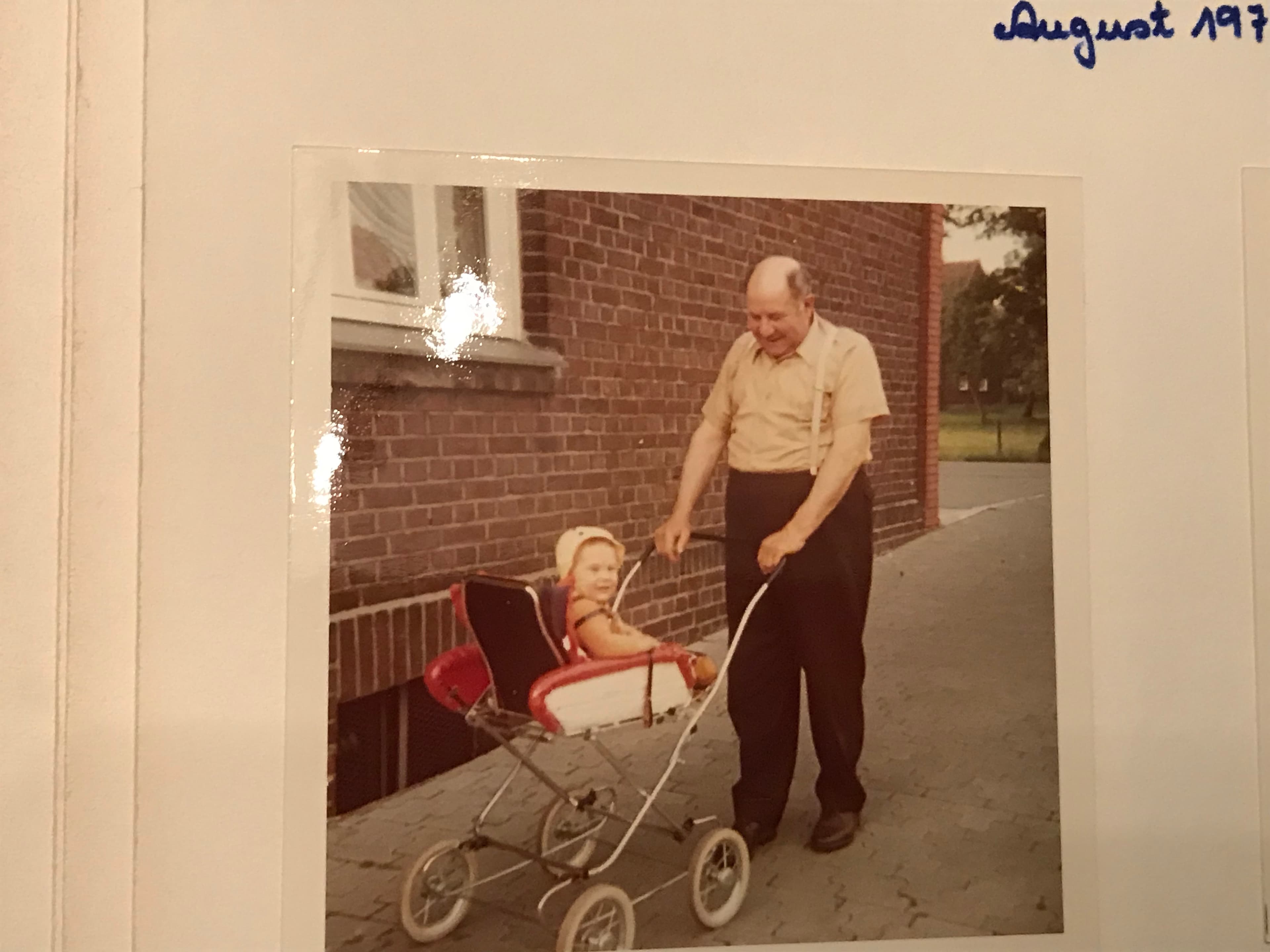 Der Großvater schiebt den kleinen Winkel im Kinderwagen über den Hof